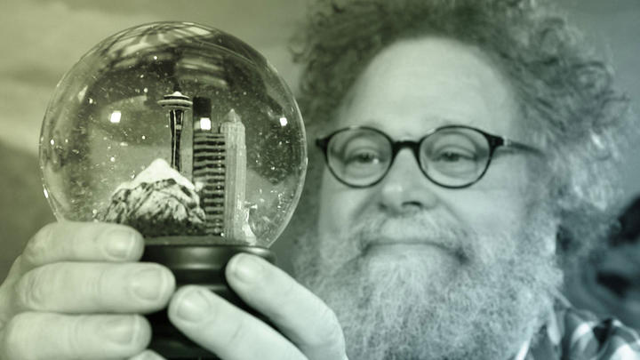 Knute Berger (of Mossback&#039;s Northwest) holds and gazes into a snowglobe containing Seattle city skyline